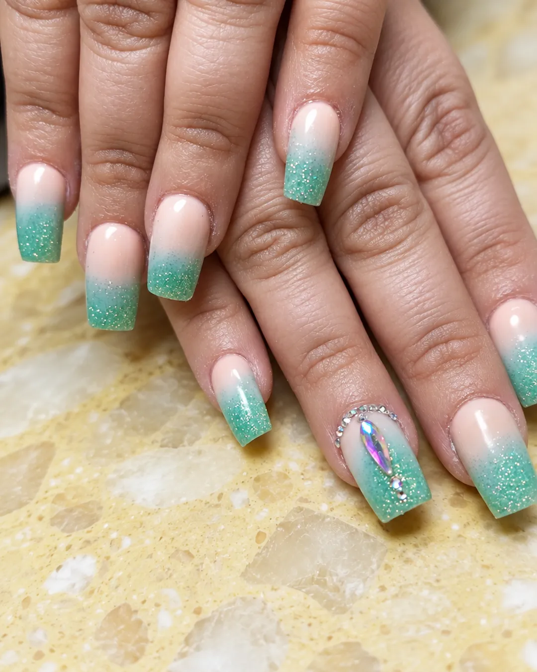 Square nails with a mint-green glitter ombre and a crystal accent