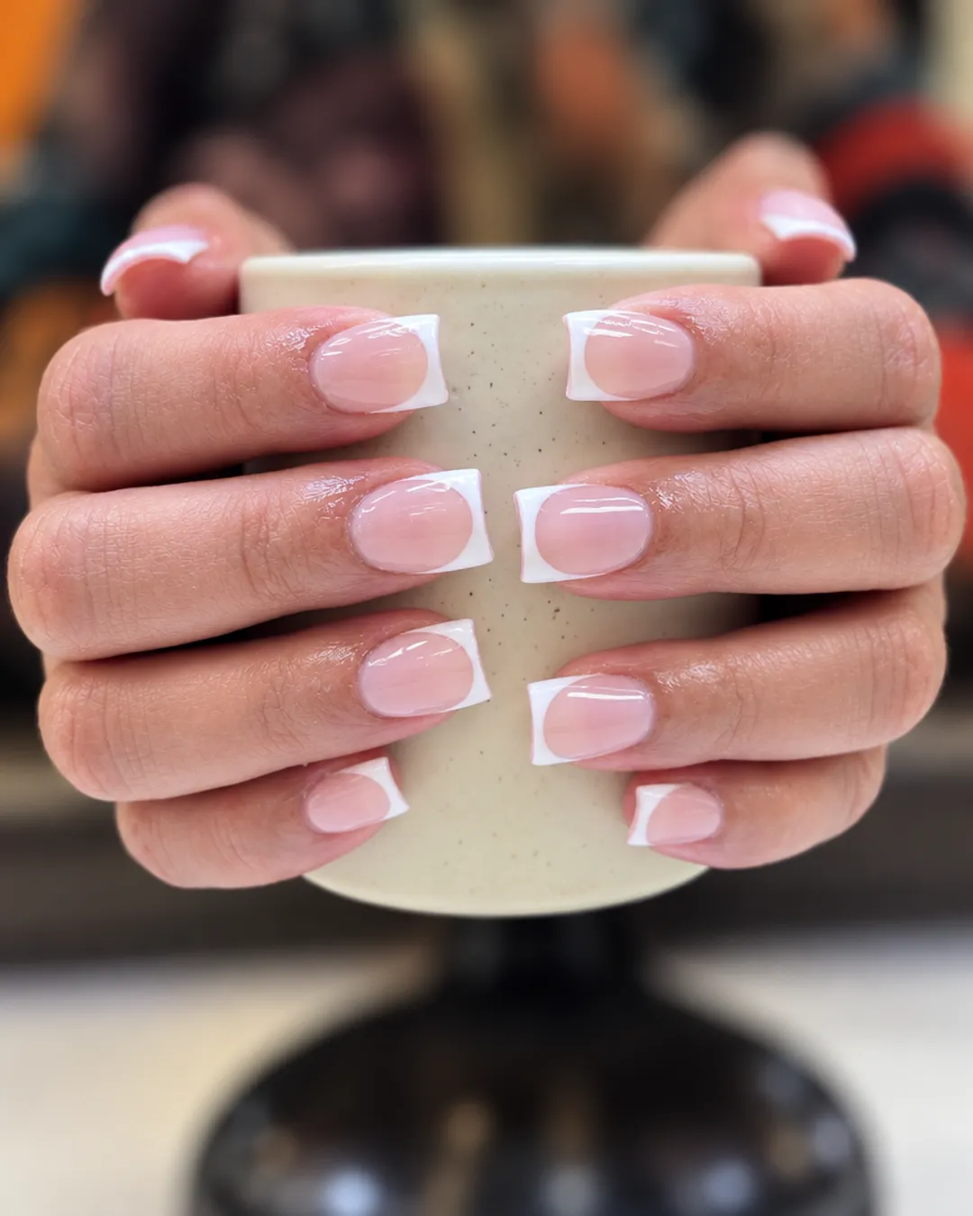 Short square French tip nails held around a coffee cup